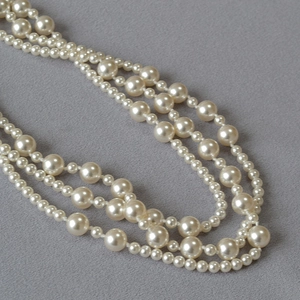 Detail of layered white faux pearl necklace showing different bead sizes on grey fabric