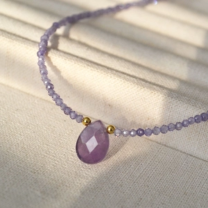 Close-up of lavender drop crystal pendant with beaded chain on a beige jewelry tray