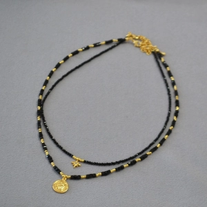 Detail of layered gold sunburst necklace with black beads and vintage coin pendant