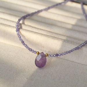 Macro detail of faceted purple gemstone teardrop pendant with small beaded chain necklace
