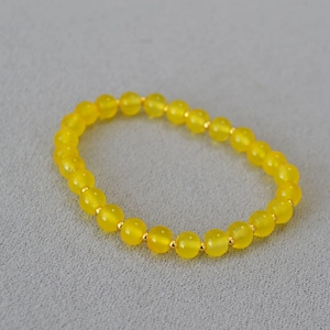 Detail of yellow agate bead bracelet with golden spacers on a textured grey surface