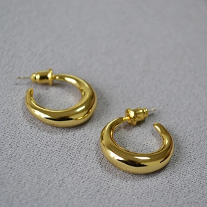 Detailed view of polished gold crescent earrings on textured grey background with butterfly back