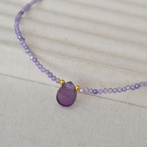 Macro view of purple faceted bead necklace with teardrop gemstone and gold accents