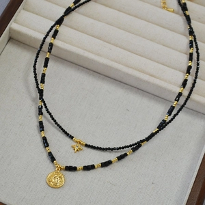 Detail of double-layered beaded necklace with gold star and coin pendants on velvet tray