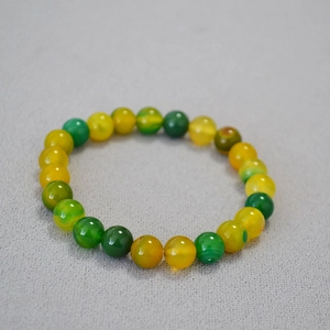 Detailed top view of polished yellow and green agate beaded stretch bracelet on grey base