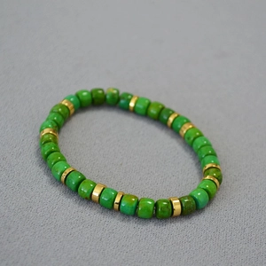 Detailed macro view of green turquoise cylinder beads and gold spacer beads on an elastic bracelet