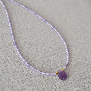 Macro detail of lavender beaded chain with teardrop-shaped amethyst gemstone pendant