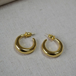 Detail of chunky gold-plated C-shaped earrings with high-polished mirror finish on fabric