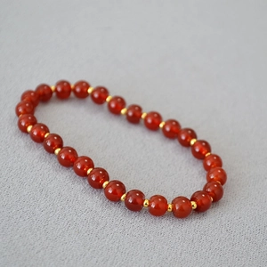 Detail of red agate bead bracelet featuring gold spacer beads on textured grey fabric