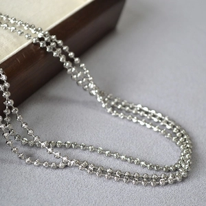 Detailed macro shot of faceted silver beaded chain necklace on textured fabric