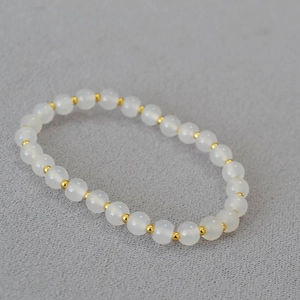 Detailed close-up of translucent white agate beads and gold spacer beads on an elastic bracelet