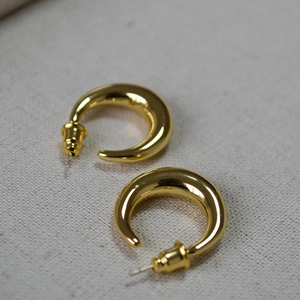 Detailed view of chunky gold-plated crescent hoop earrings on a light grey textured fabric