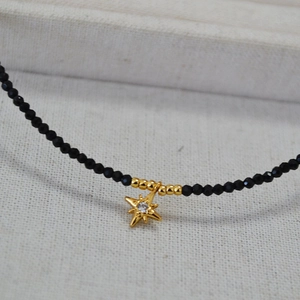 Detailed view of a black beaded necklace featuring a gold star pendant with a center crystal
