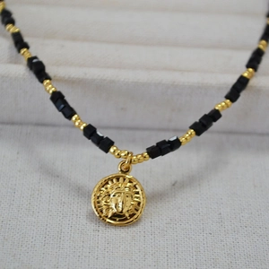 Detail of beaded necklace with gold Medusa relief pendant and black cube beads