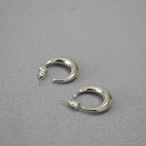 Macro detail of thick crescent-shaped silver stud earrings on grey fabric background