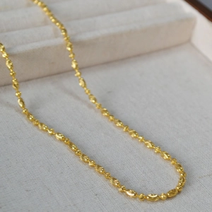 Detail view of gold beaded chain featuring textured oval links and polished round beads