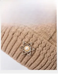 Detail of khaki knit winter hat featuring an elegant floral brooch with pearl and crystals