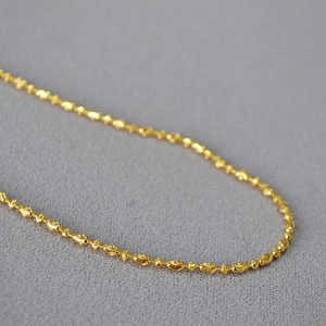 Macro view of gold plated bead chain necklace showing intricate texture on gray fabric
