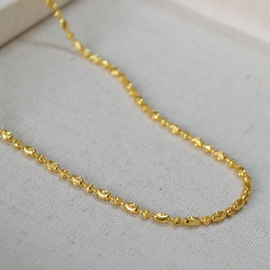 Macro detail of polished gold-plated beaded chain showing intricate texture and luxury finish