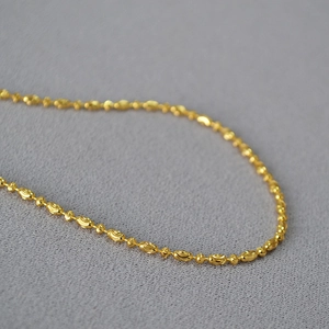 Macro shot of gold-plated beaded chain featuring olive-shaped beads and fine texture