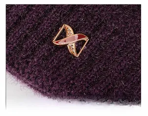 Detail of purple knit hat featuring a luxury gold metal emblem with rhinestone accents