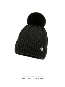 Detail of black cable knit beanie with large faux fur pompom and metal H logo badge