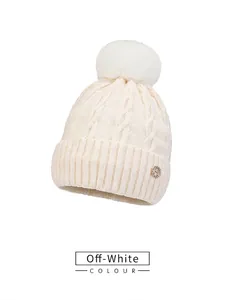 Detailed close-up of beige cable knit beanie featuring large pompom and gold H-logo charm