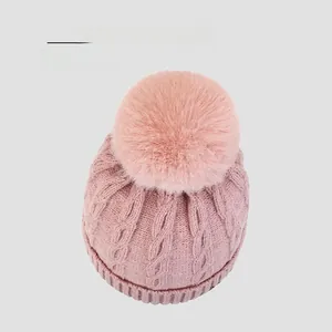 Detailed top view of pink knit hat with a large fluffy pompom and cable knit texture