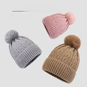 Detailed flat lay of knit beanies in pink, grey and khaki with faux fur pom poms