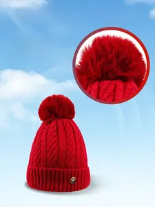 Close-up of chunky cable knit texture with large faux fur pom-pom and gold logo badge