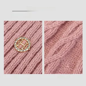 Close-up of pink cable knit winter hat featuring a luxury gold crystal H logo detail