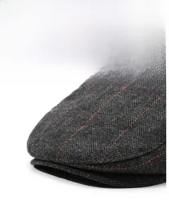 Detailed close-up of dark grey herringbone flat cap with fine red plaid wool texture