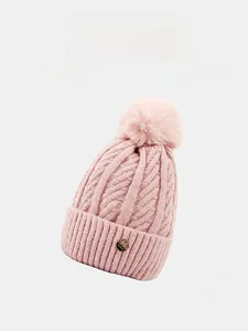 Detail of pink cable knit beanie featuring a fluffy pompom and gold logo badge