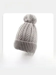 Detail of grey knitted beanie featuring a fluffy faux fur pom-pom and metal logo badge
