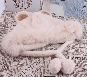 Détail du bonnet d'ours en peluche beige avec pompons moelleux sur fond de journal