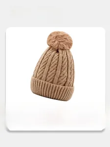 Detailed view of the brown knit beanie with soft plush lining and pompom decoration