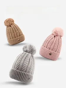 Detailed knit texture of cable-knit beanies with faux fur pom-poms in three colors