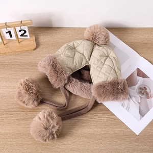 Detail of khaki earflap hat showing quilted texture, plush brown fur and soft pom-poms