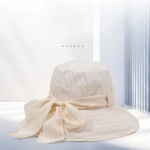 Detail of light beige sun hat showing fine gold stripes and elegant ribbon bow decoration