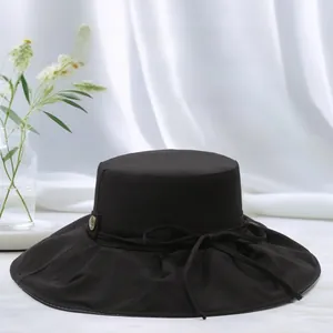 Close-up of black wide-brim sun hat featuring a delicate bow and gold metal buckle detail