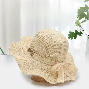 Detail of beige straw sun hat featuring wavy brim and elegant bow with gold buckle accent