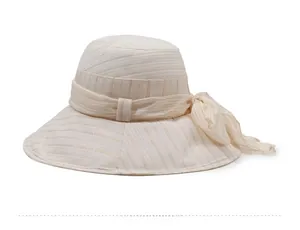 Detail view of beige sun hat with gold stripes and a soft bow on the side