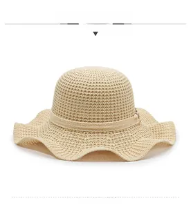 Front view of beige knit sun hat with wavy brim, ribbon detail and metal pendant
