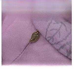 Detailed close-up of purple fabric texture with a golden leaf charm on the sun hat