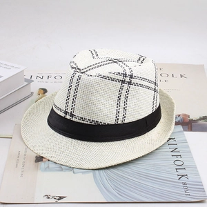 Détail d'un chapeau de paille blanc à motif écossais noir posé sur des magazines de mode