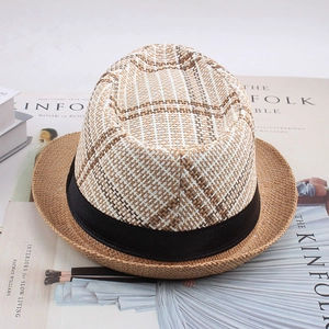 Vue de dessus d'un chapeau fedora tressé avec couronne à carreaux et ruban noir sur magazine