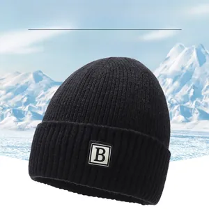 Detailed knit texture of a black winter beanie with letter B patch and snowy peak background