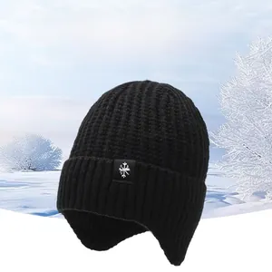 Macro detail of black knitted winter beanie featuring ear flaps and snowflake patch