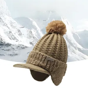 Detail of khaki fleece-lined knit hat with earflaps and faux fur pom against snow mountain
