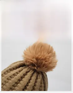 Detail of a brown thick knit beanie featuring a large matching faux fur pom-pom ball